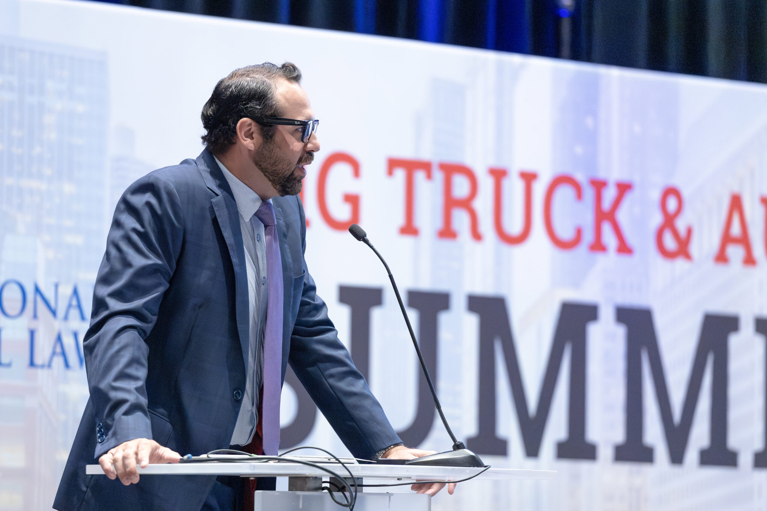 an image of a man presenting in front of a sign that reads "big truck & auto summit"